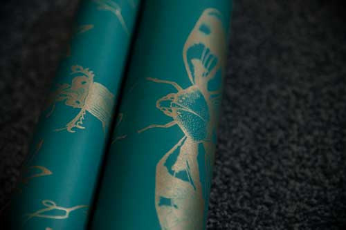 A roll of entomology inspired wallpaper with silver cicadas against a blue background